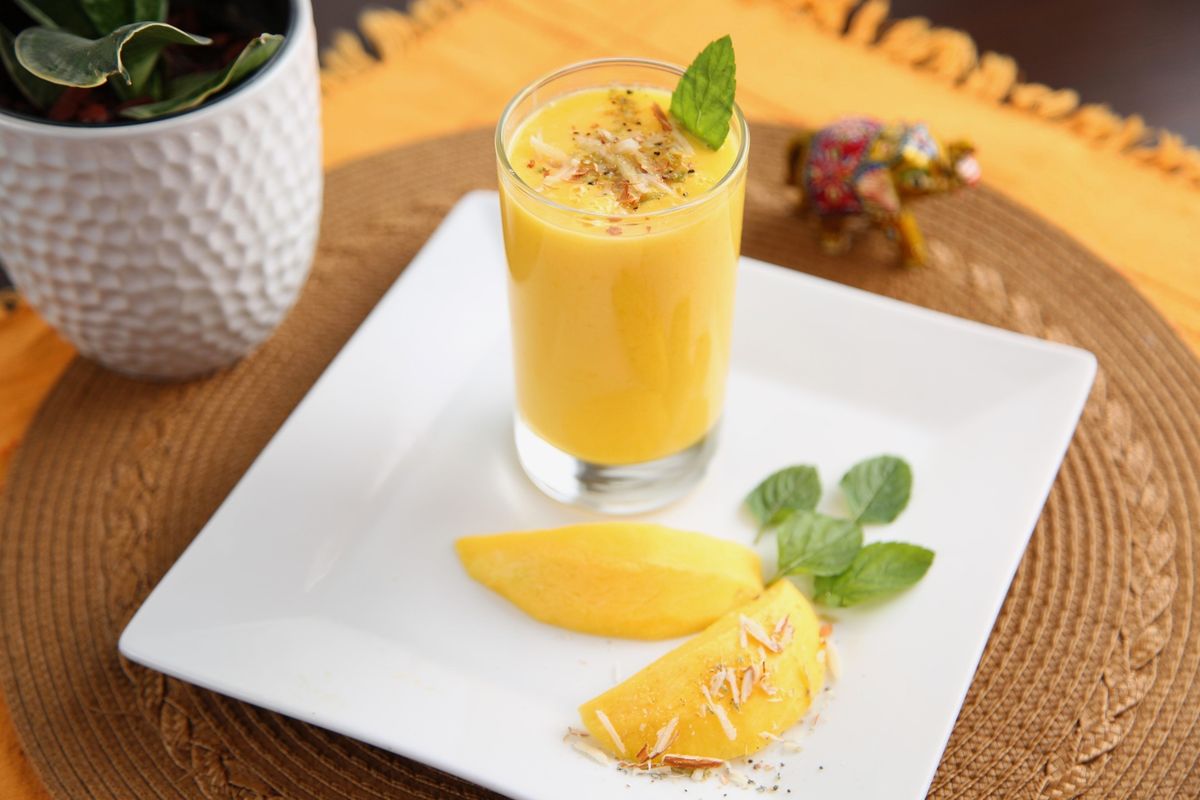 A glass of mango lassi with fresh mango and mint