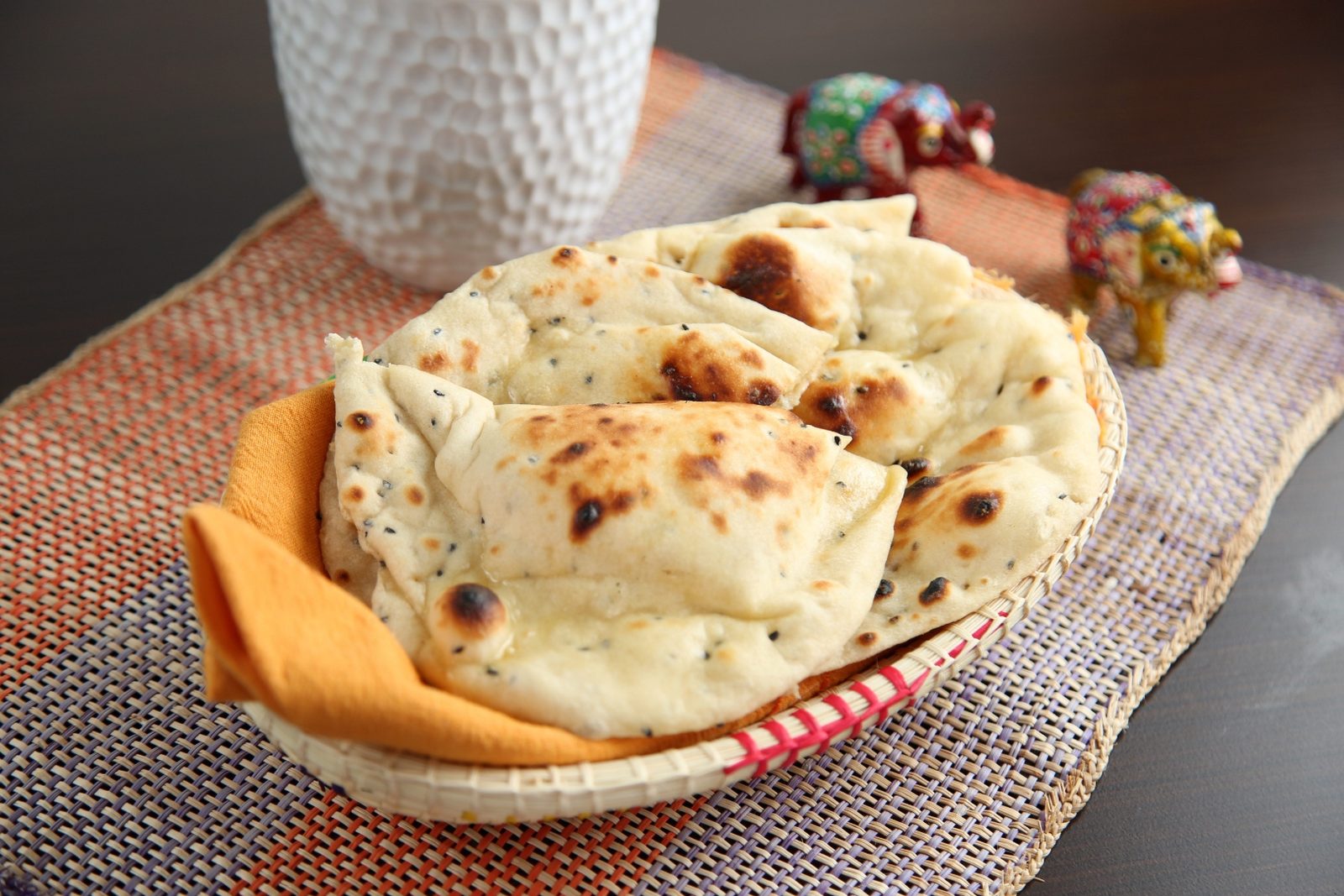 A basket of golden, char-flecked naan bread wrapped in an orange napkin at Mantraa